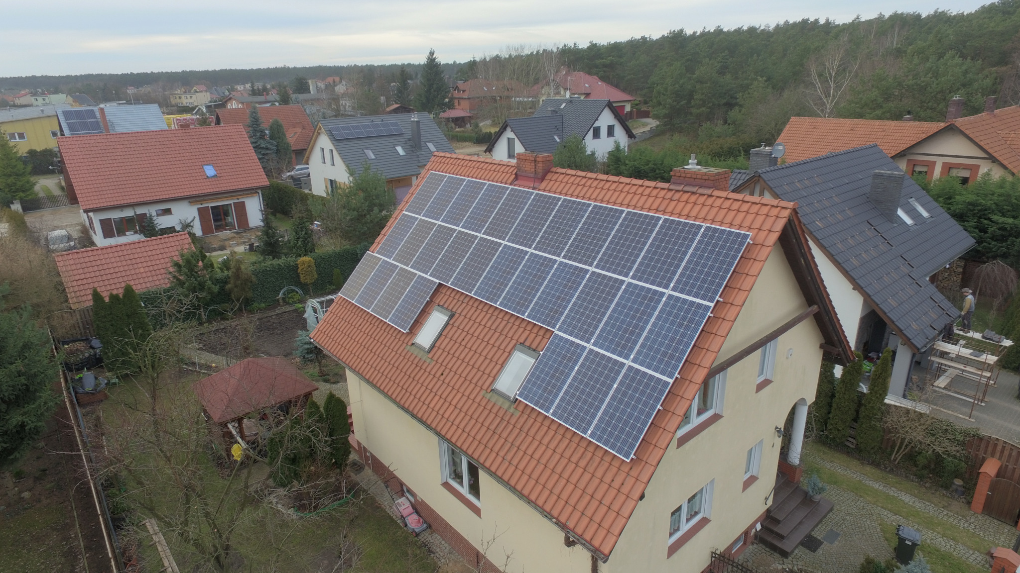 Dom jednorodzinny z panelami słonecznymi na pomarańczowym dachu w Wągrowcu, widok z góry, pochmurne niebo.