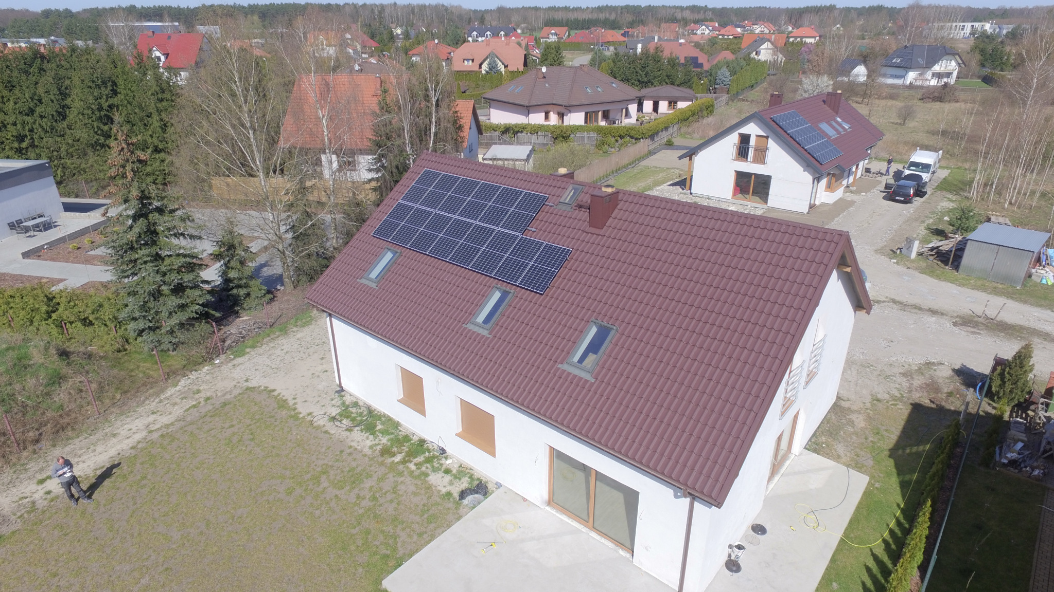 Widok z drona na dom jednorodzinny z brązowym dachem i panelami słonecznymi, w tle zabudowa Osielska i las.