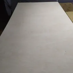 Jasna płyta sklejki o delikatnym wzorze drewna, leżąca na stole w warsztacie.