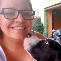 Uśmiechnięta kobieta w okularach pozuje do selfie z psem o czarno-białym umaszczeniu, w tle widoczna zieleń i grill.