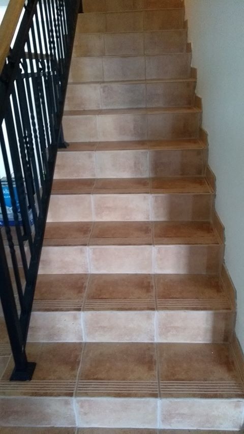 Schody wyłożone brązowymi płytkami ceramicznymi z antypoślizgowymi rowkami, widoczne czarne metalowe poręcze.