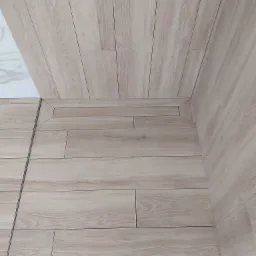 Beżowe płytki imitujące drewno ułożone na podłodze i ścianie, z widocznymi fugami i narożnikiem wykończonym pod kątem 45 stopni.