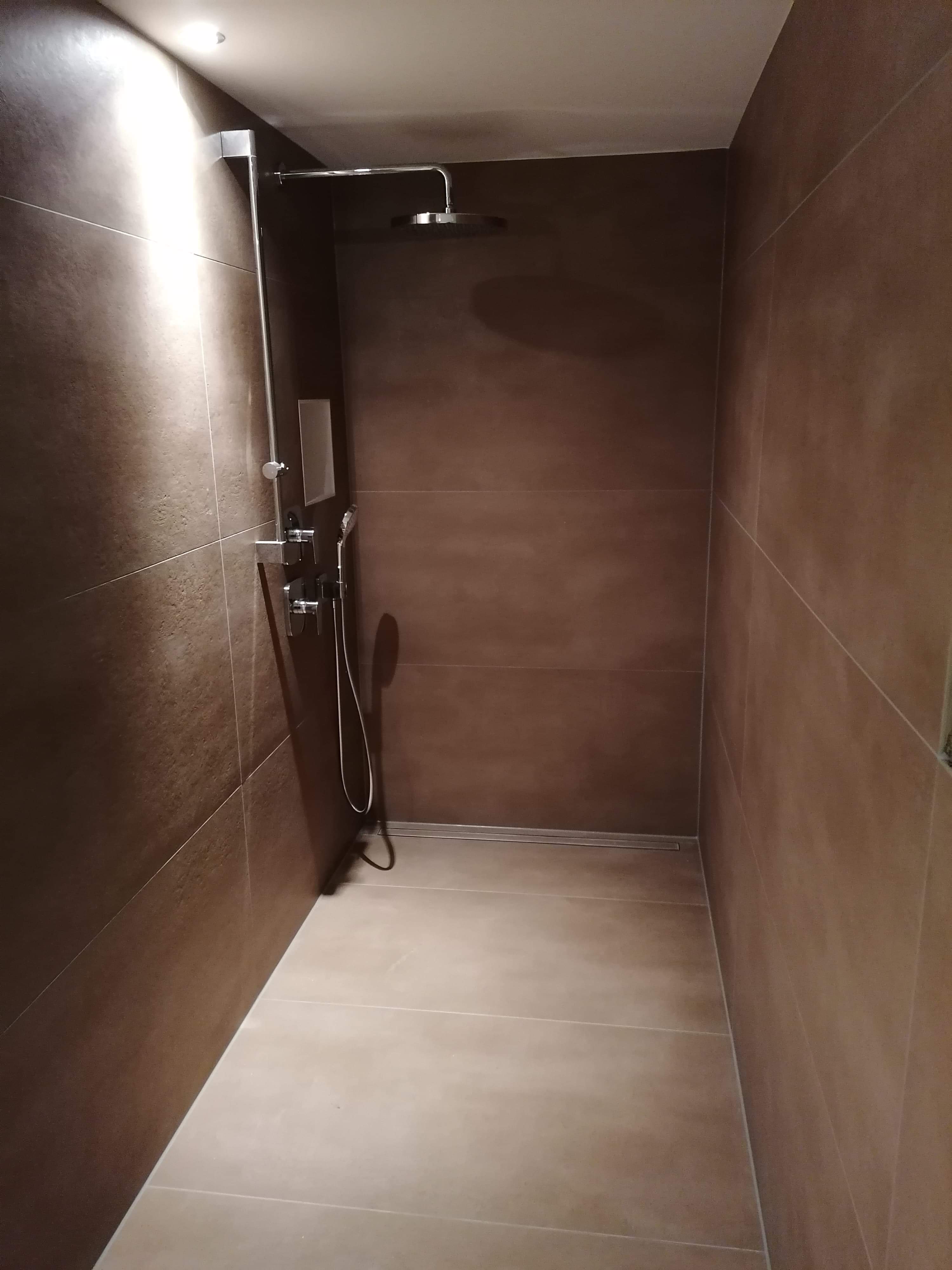 Kabina prysznicowa wyłożona brązowymi, podłużnymi płytkami, z odpływem liniowym w podłodze i nowoczesną armaturą.