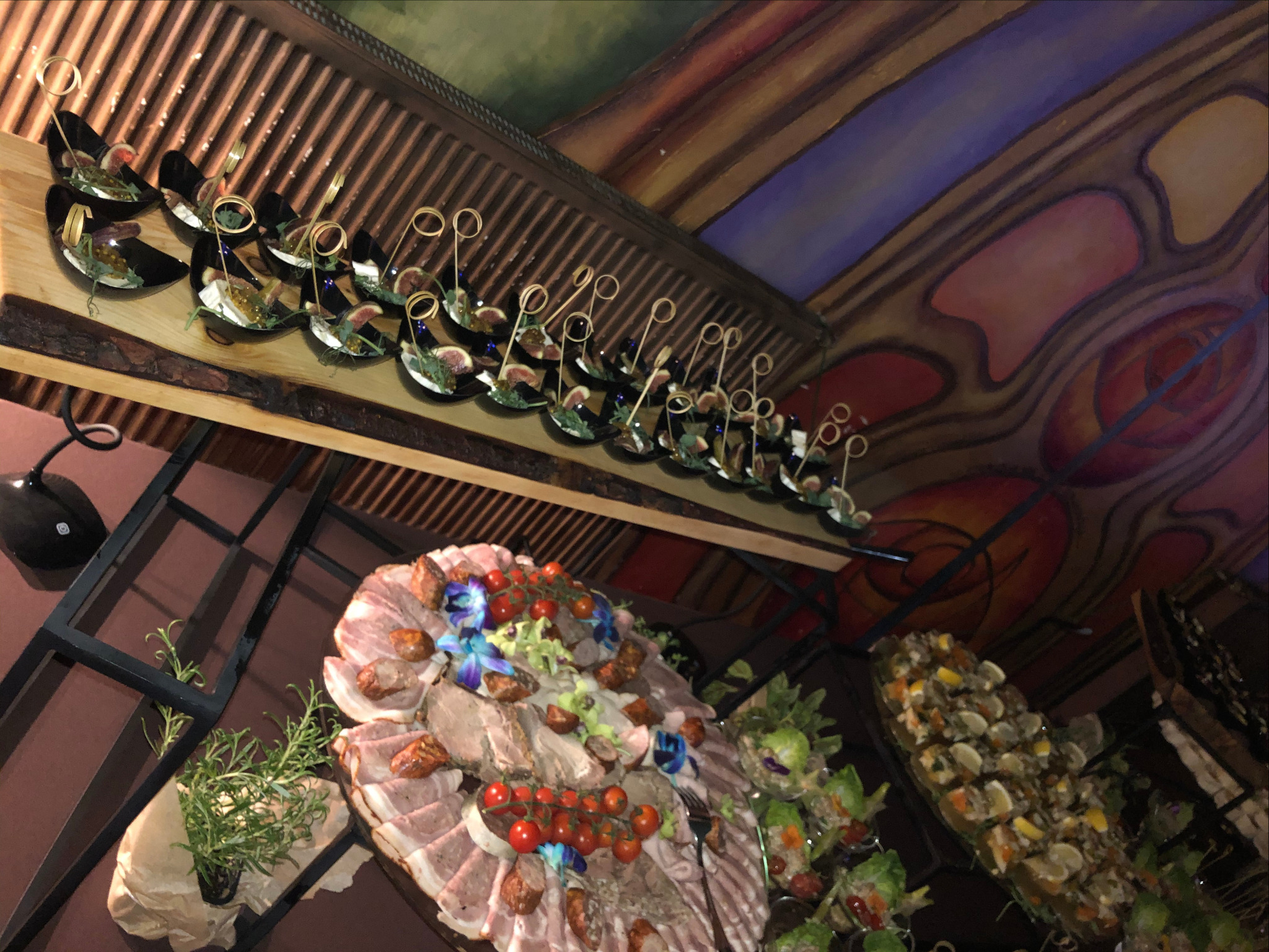 Dekoracyjnie podane przekąski na drewnianych deskach i w czarnych łódeczkach, z widocznym sufitem w stylu art deco.