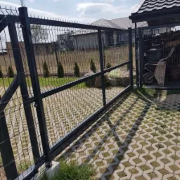 Nowoczesne, grafitowe ogrodzenie z siatki z bramą przesuwną na posesji z ażurową kostką brukową, widok z zewnątrz.