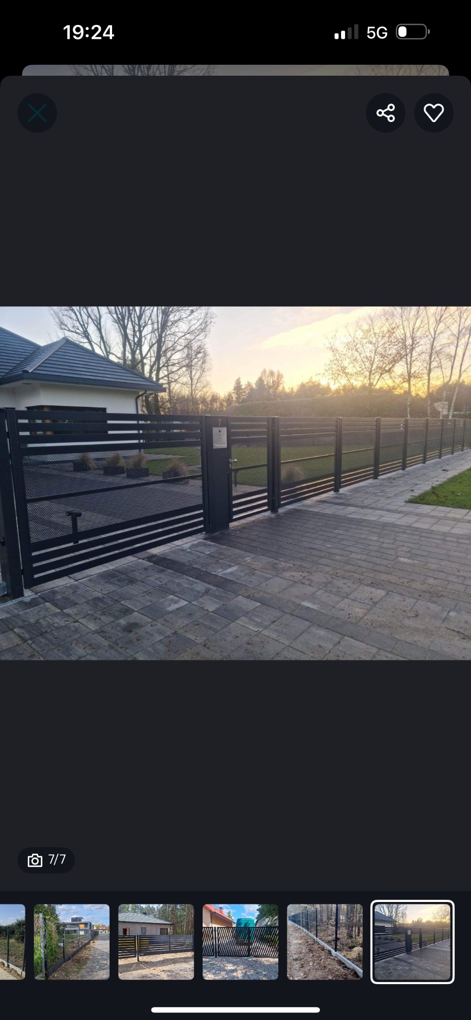 Nowoczesna, czarna brama wjazdowa z perforowanym wypełnieniem i furtką, z numerem domu, na tle kostki brukowej i domu jednorodzinnego o zmierzchu.