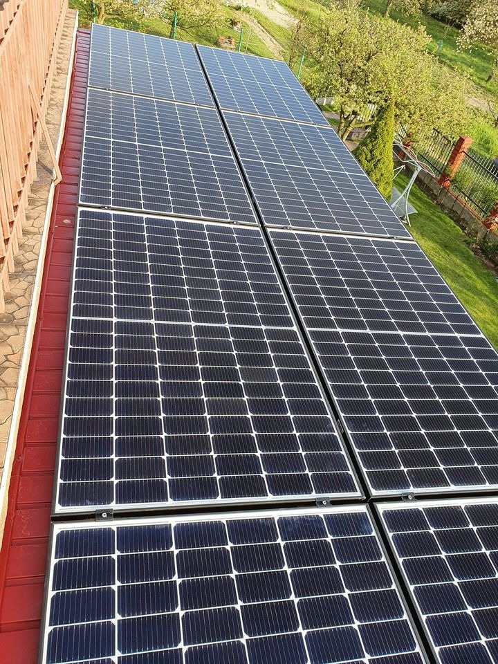 Panele słoneczne na czerwonym dachu, widok z góry, w tle zieleń ogrodu i drzewa.