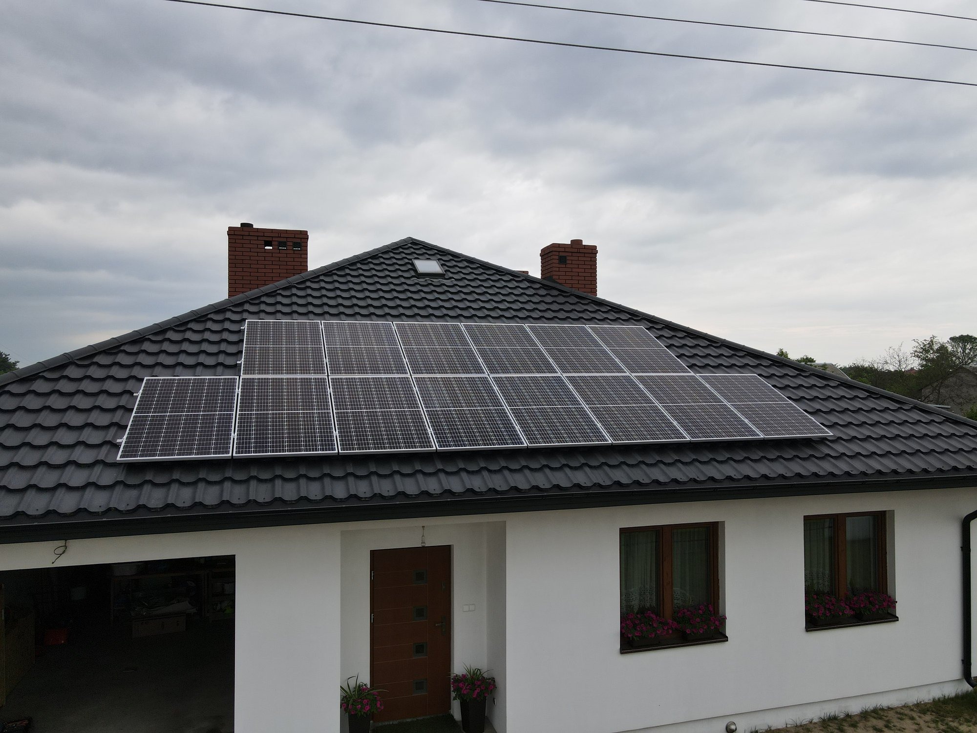 Panele słoneczne na dachu nowoczesnego domu z szarej dachówki, widok z dołu, pochmurne niebo w tle.