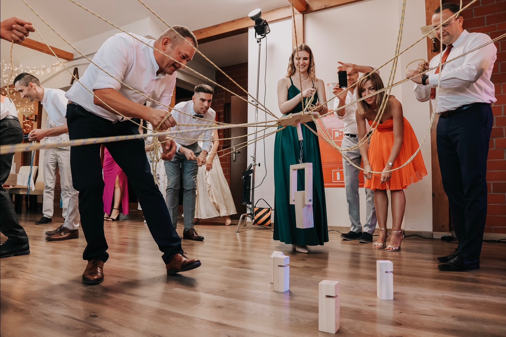 Uczestnicy imprezy integracyjnej rozwiązują zadanie z linami, drewniane elementy na podłodze, gra zespołowa.