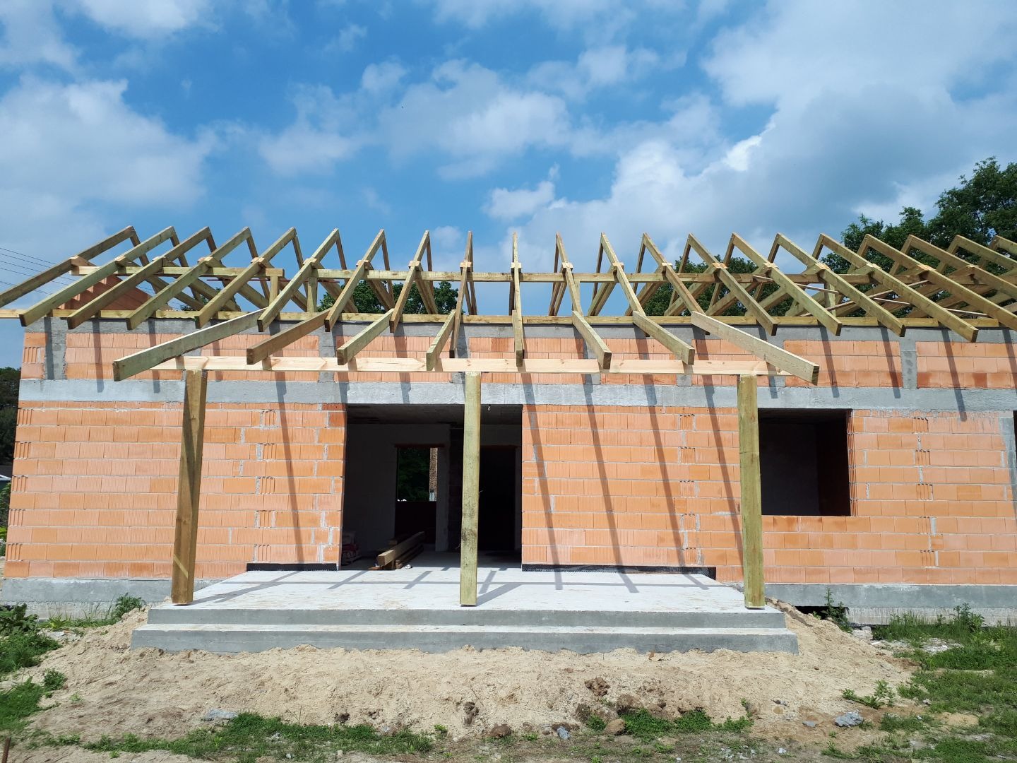 Wznoszenie drewnianej konstrukcji dachu na murowanym budynku z czerwonej cegły, widok na niebo z chmurami.