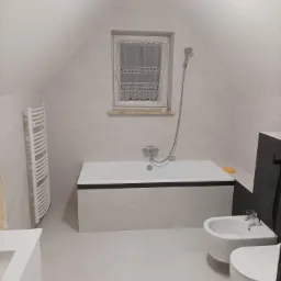 Jasna łazienka na poddaszu z białą wanną obudowaną płytkami, grzejnikiem drabinkowym, bidetem i toaletą.