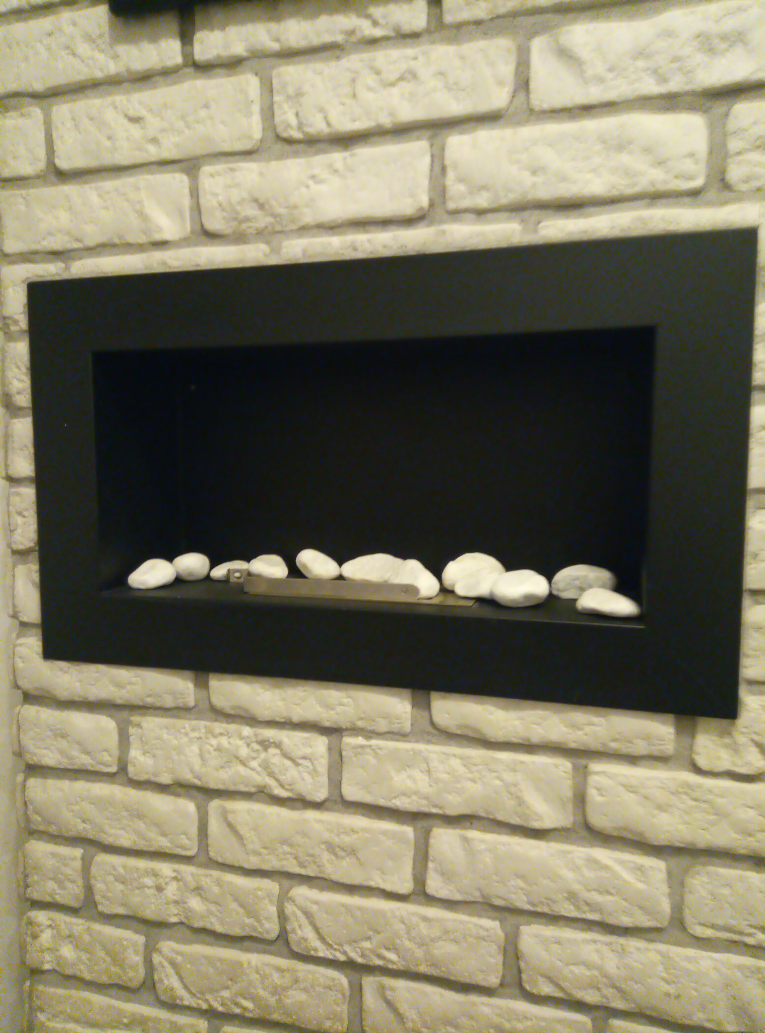 Wnęka w ścianie wyłożonej białymi cegłami, z czarną ramą i rzędem dekoracyjnych białych kamieni na dolnej półce.