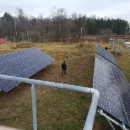 Instalacja paneli słonecznych 33kWp w Kielcach na nierównym terenie. Widoczne panele, konstrukcja wsporcza, oraz dwie osoby przy pracy.