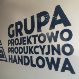 Niebieski napis 'GRUPA PROJEKTOWO PRODUKCYJNO HANDLOWA' oraz logo GPPPH umieszczone na jasnej ścianie, wykonane z błyszczącego tworzywa.