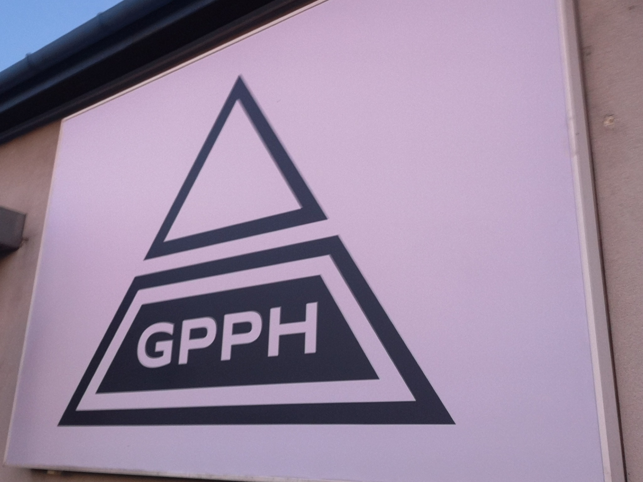 Szyld z logo firmy GPPH, umieszczony na budynku, przedstawiający trójkąt z wpisanym skrótem nazwy.