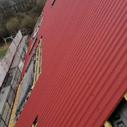 Czerwony dach z blachy trapezowej w trakcie montażu w Białymstoku, widoczne łaty i kontrłaty, a także fragment rusztowania.