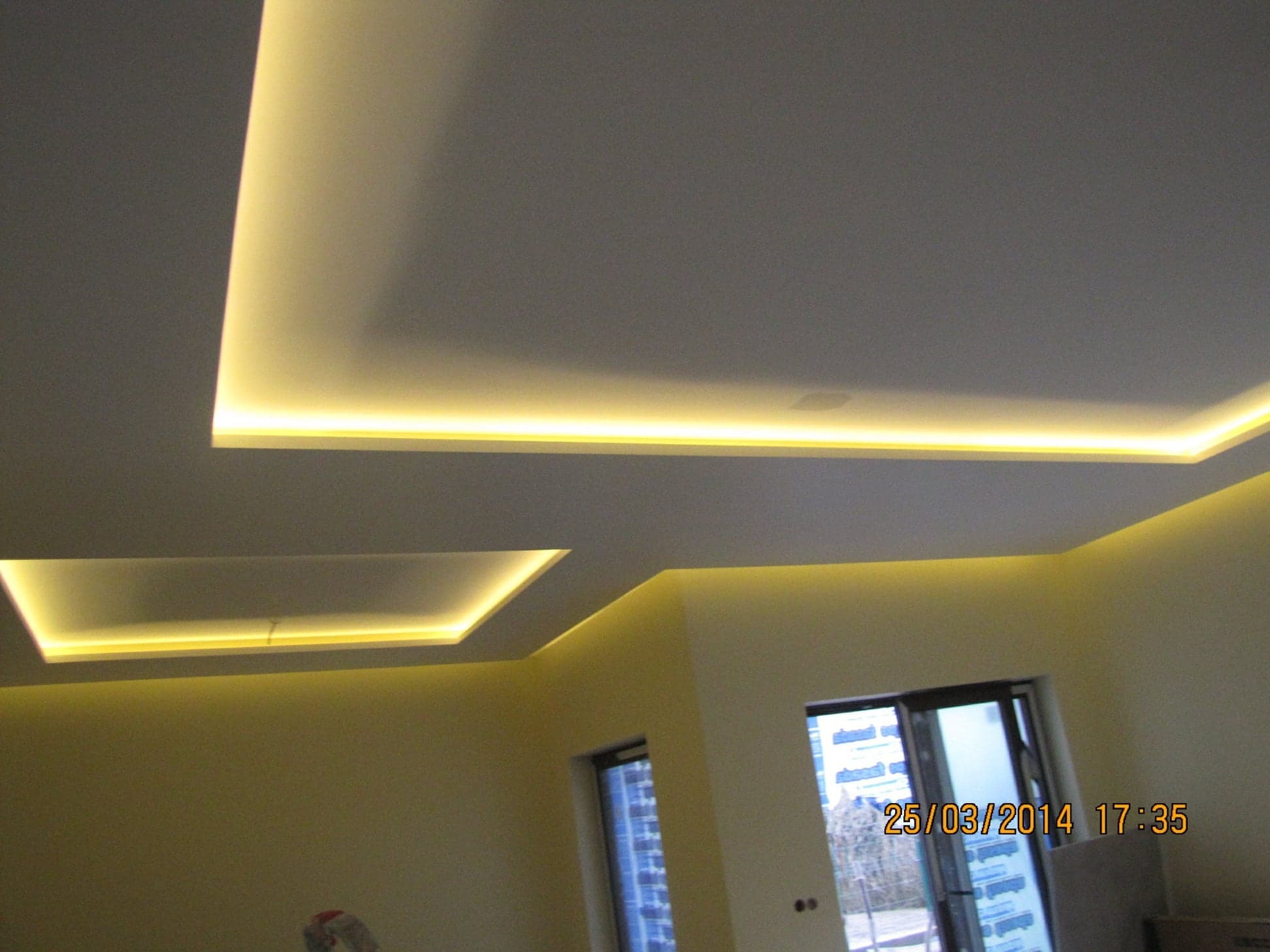 Sufit podwieszany z oświetleniem LED w kształcie prostokątów, widoczne dwa okna z widokiem na zewnątrz.