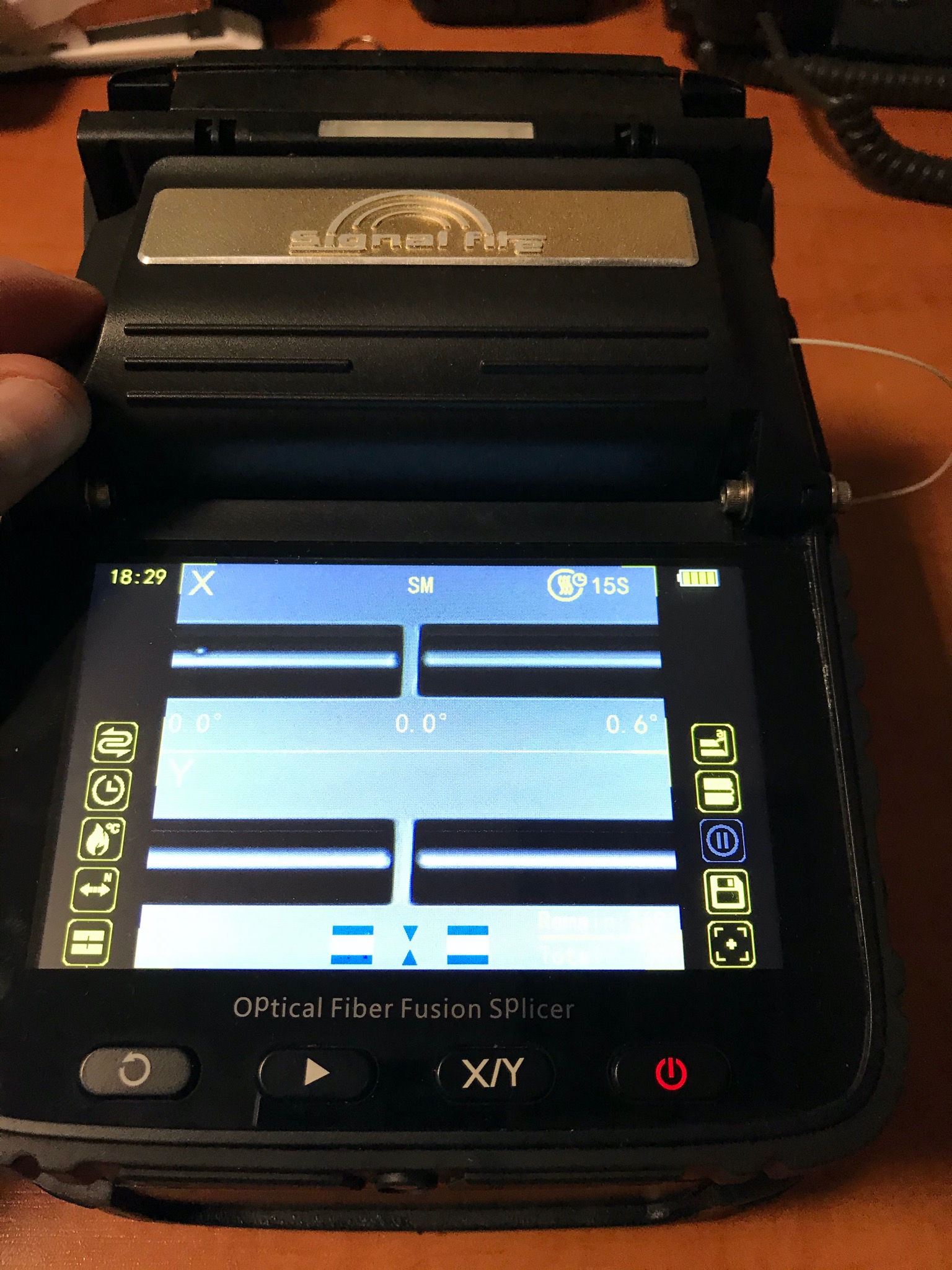 Zbliżenie na spawarkę światłowodową z widocznym ekranem wyświetlającym parametry spawania, obok wystający fragment włókna światłowodowego.