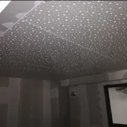 Sufit z płyty perforowanej w trakcie montażu, widoczne łączenia płyt i surowe ściany przygotowane do dalszych prac wykończeniowych.