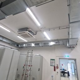 D.I.E. Wasinski Krzysztof - Instalacja wentylacji i klimatyzacji w pomieszczeniu technicznym z drabiną, widoczne kanały wentylacyjne, klimatyzator kasetonowy i szafy elektryczne.