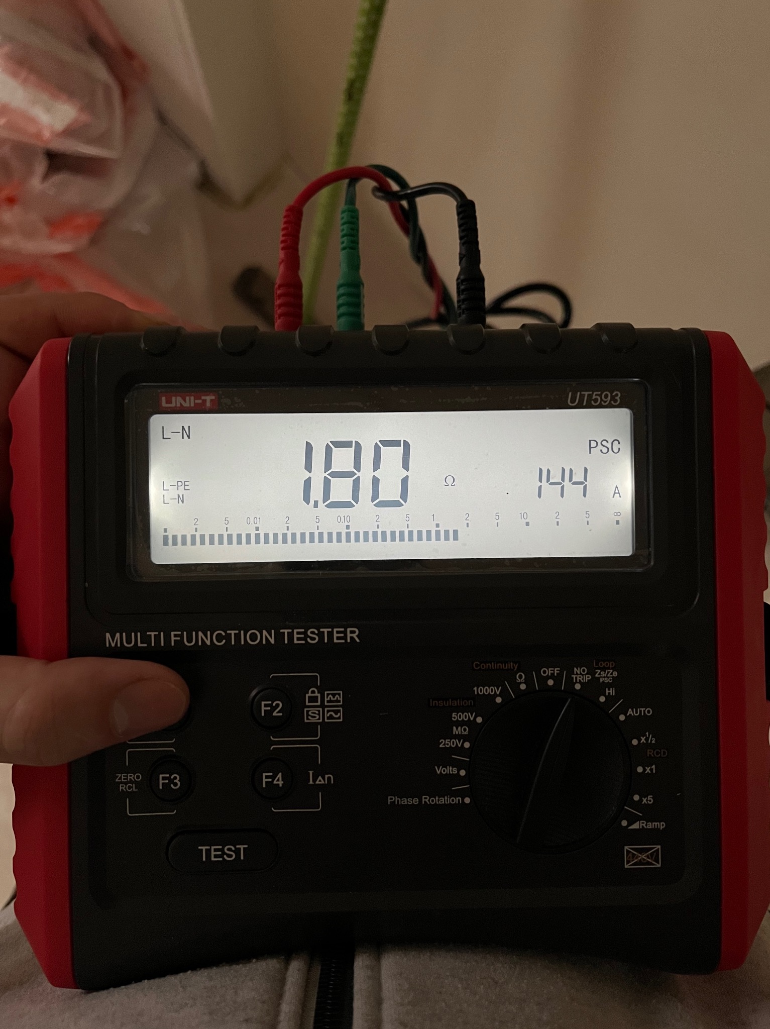 Miernik wielofunkcyjny UNI-T UT593 z podłączonymi przewodami pomiarowymi, wskazujący rezystancję 1.80 omów i prąd zwarciowy 144 ampery, używany do weryfikacji instalacji elektrycznej.