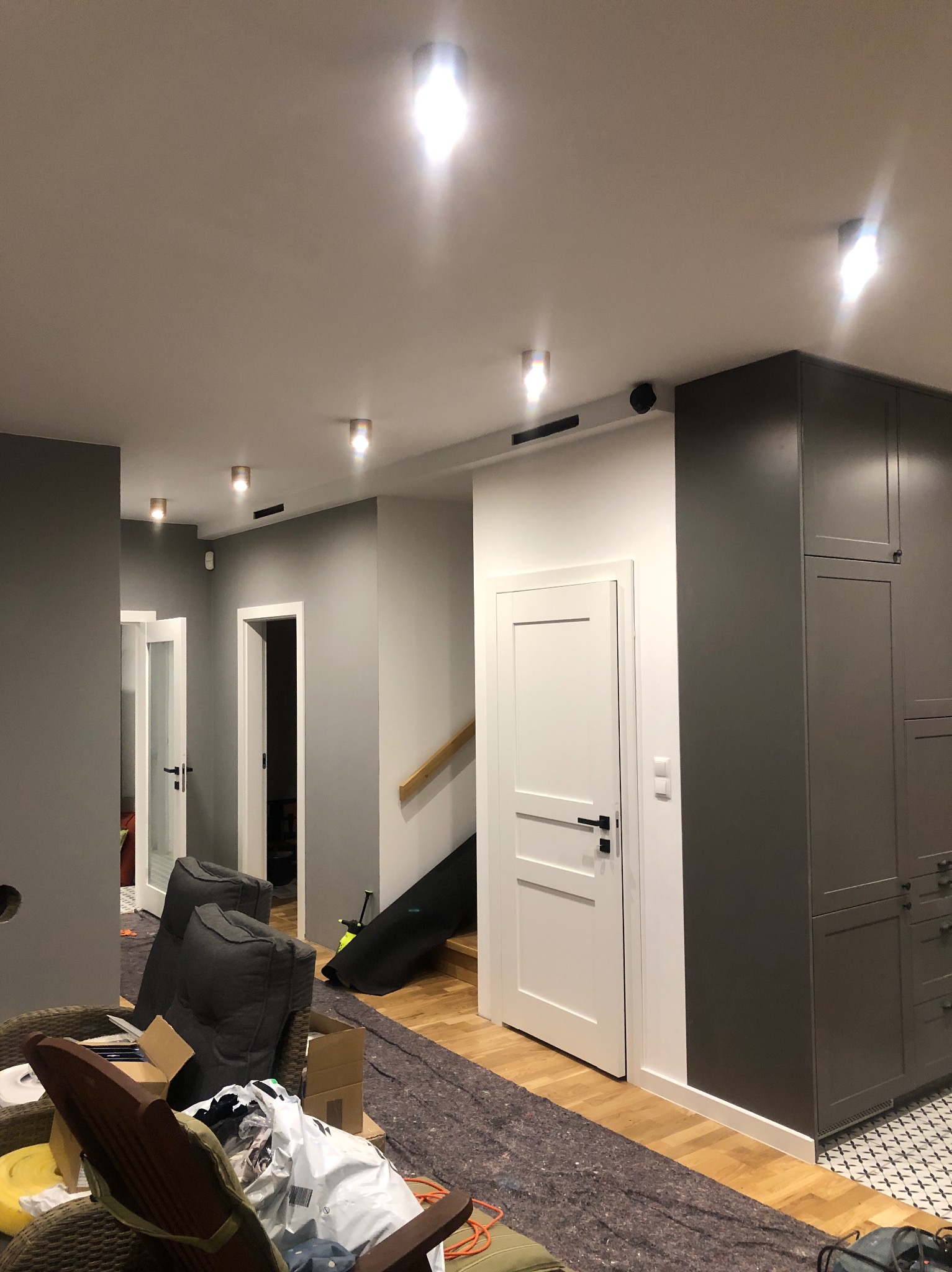 Korytarz w trakcie remontu z widocznymi punktami oświetleniowymi w suficie, zabezpieczoną podłogą, meblami i kartonami.