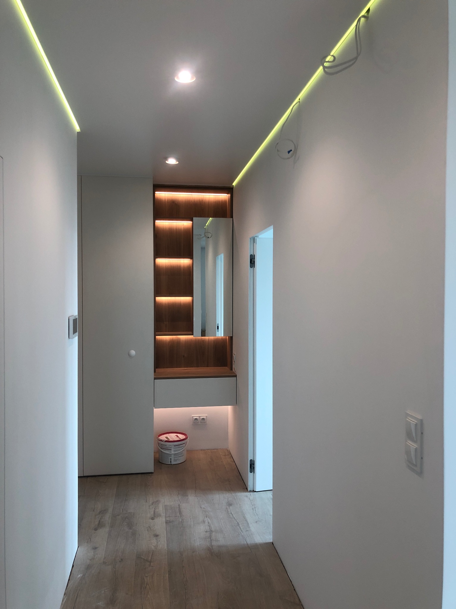 Nowoczesny korytarz z oświetleniem LED podsufitowym i wbudowaną szafą z lustrem, widoczne przewody elektryczne wystające z podsufitki.
