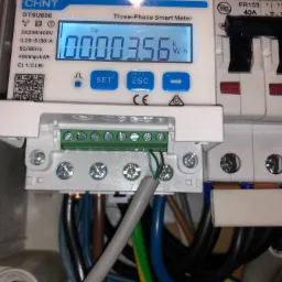 Szczegółowe zbliżenie na trójfazowy inteligentny licznik energii CHNT DTSU666 z wyświetlaczem wskazującym 00003.56 kWh, podłączony do instalacji elektrycznej z widocznymi przewodami...
