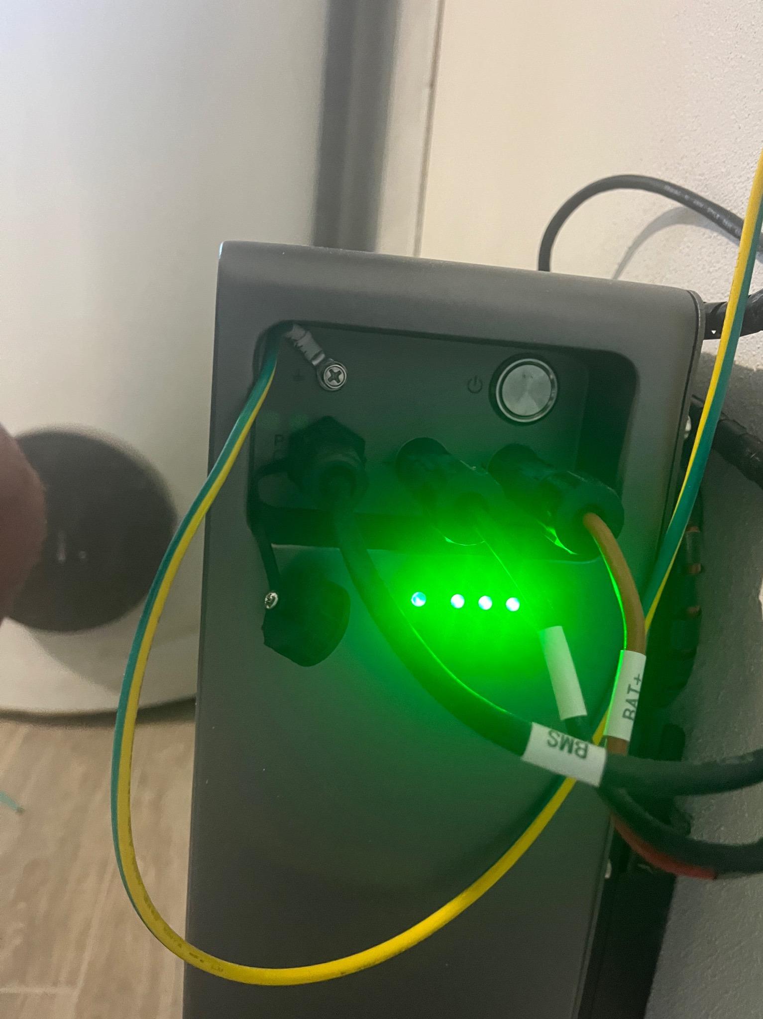 Szary moduł z podłączonymi kablami (BAT+, BMS) i świecącymi na zielono diodami LED, sugerujący działanie systemu. Widoczne złącza i przewody elektryczne.