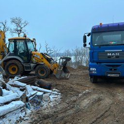 K.N-TURBO TRANS-KOP Kamil Napiórkowski - Żółta koparko-ładowarka JCB i niebieski MAN na błotnistym terenie z gruzem. Widoczne ślady opon. Zimowa sceneria, pochmurne niebo. Na szybie MAN naklejka z imieniem kierowcy.