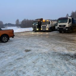 K.N-TURBO TRANS-KOP Kamil Napiórkowski - Trzy ciężarówki Scania i MAN stoją na zaśnieżonym placu budowy w zimowy dzień. Pomarańczowy pickup Ford Ranger częściowo widoczny z lewej strony kadru.