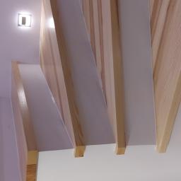 NowaMal Krzysztof Nowakowski Wykończenia Remonty Stolarstwo - Sufit z dekoracyjnymi, drewnianymi belkami o jasnym odcieniu drewna, ułożonymi pod kątem, z oświetleniem punktowym w tle, widok z dołu.