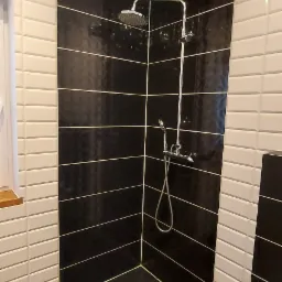 Nowoczesna kabina prysznicowa z czarnymi i białymi płytkami ułożonymi w poziome pasy, chromowana armatura, odpływ liniowy z dekoracyjnym wzorem.