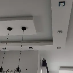 Wielopoziomowy sufit podwieszany z płyt kartonowo-gipsowych z oświetleniem punktowym i wiszącymi lampami, dekoracyjna ściana z cegły.