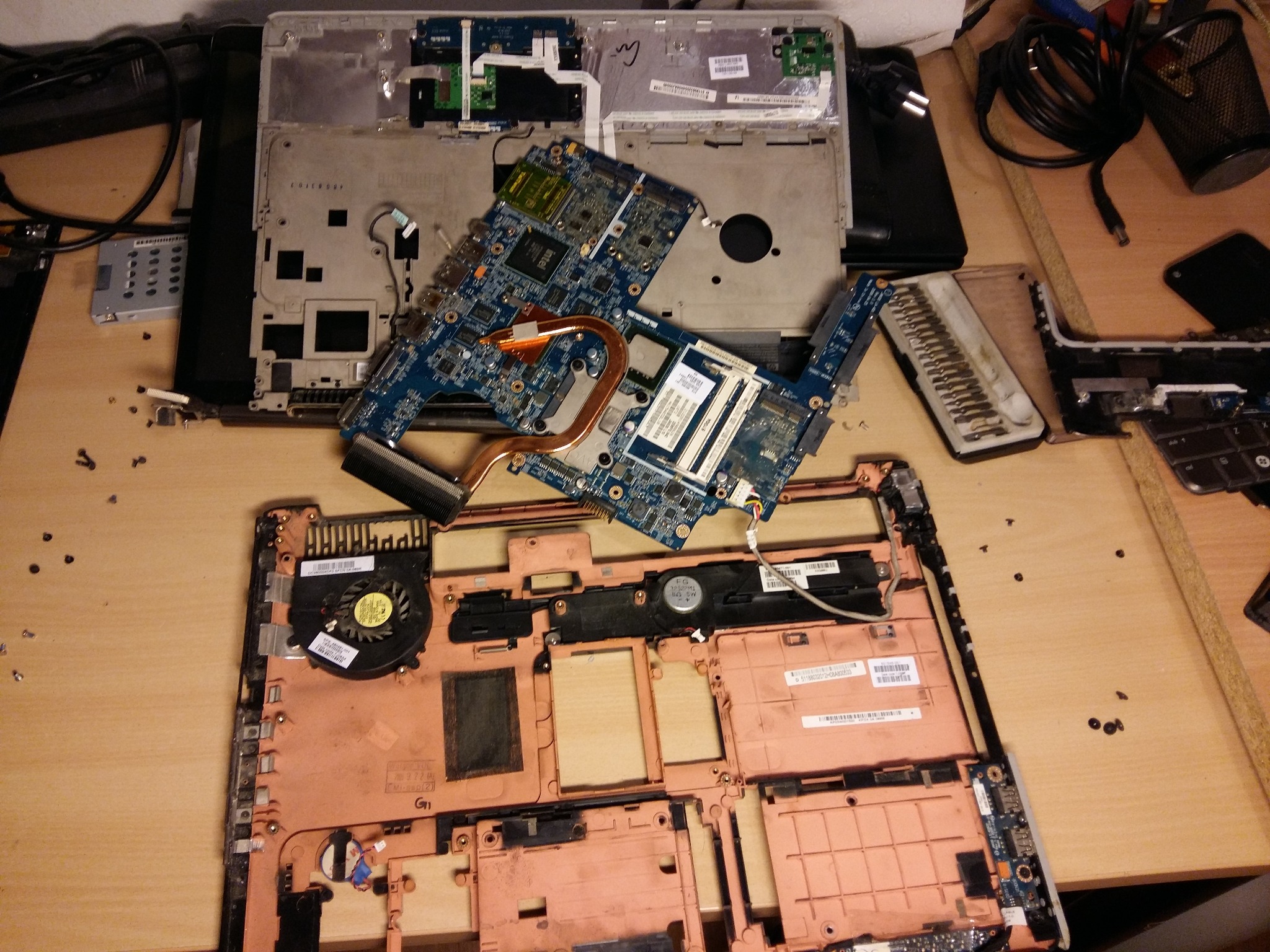 Rozłożony laptop na stole roboczym, widoczne płyty główne, wentylator, obudowa, śrubokręty i drobne śrubki.