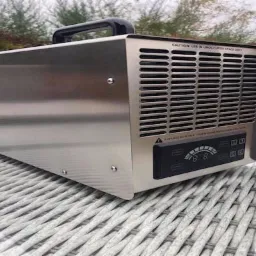 Generator ozonu w metalowej obudowie z czarnym panelem sterowania, umieszczony na plecionym stole na zewnątrz.