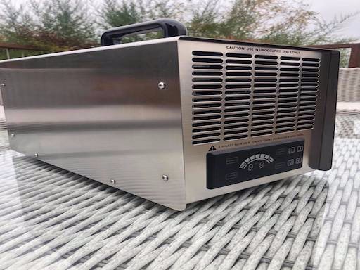 Generator ozonu w metalowej obudowie z czarnym panelem sterowania, umieszczony na plecionym stole na zewnątrz.
