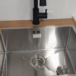 Dariusz Wiśniewski - Nowoczesna, czarna bateria kuchenna nad zlewem ze stali nierdzewnej, zamontowana w Grodzisku Mazowieckim. Widoczne krople wody w zlewie.