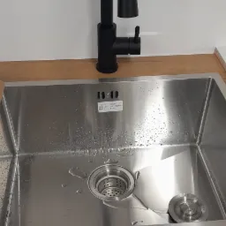 Nowoczesna, czarna bateria kuchenna nad zlewem ze stali nierdzewnej, zamontowana w Grodzisku Mazowieckim. Widoczne krople wody w zlewie.