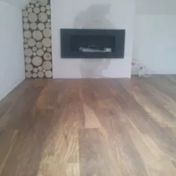 Ułożone panele podłogowe w pokoju z dekoracyjnym panelem z drewna i nowoczesnym kominkiem.