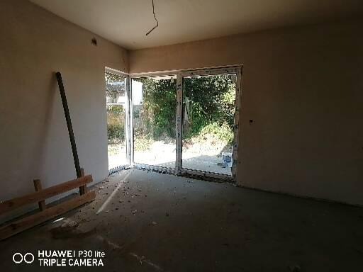 Wnętrze pokoju w stanie surowym po remoncie, z dużym oknem balkonowym, widoczne ślady gruzu i pyłu na podłodze, ściany przygotowane do malowania.