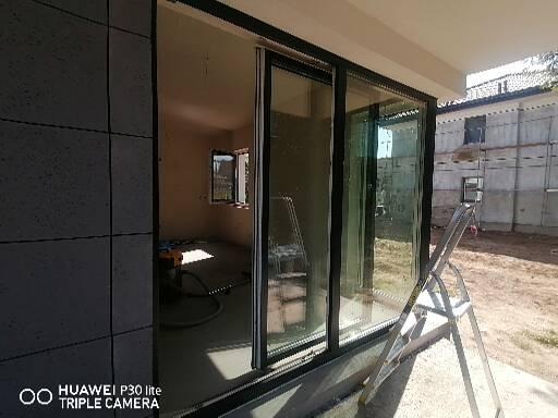 Duże przesuwne okno tarasowe z czarną ramą, widok na wnętrze w trakcie sprzątania po remoncie, drabina oparta o szybę na zewnątrz.