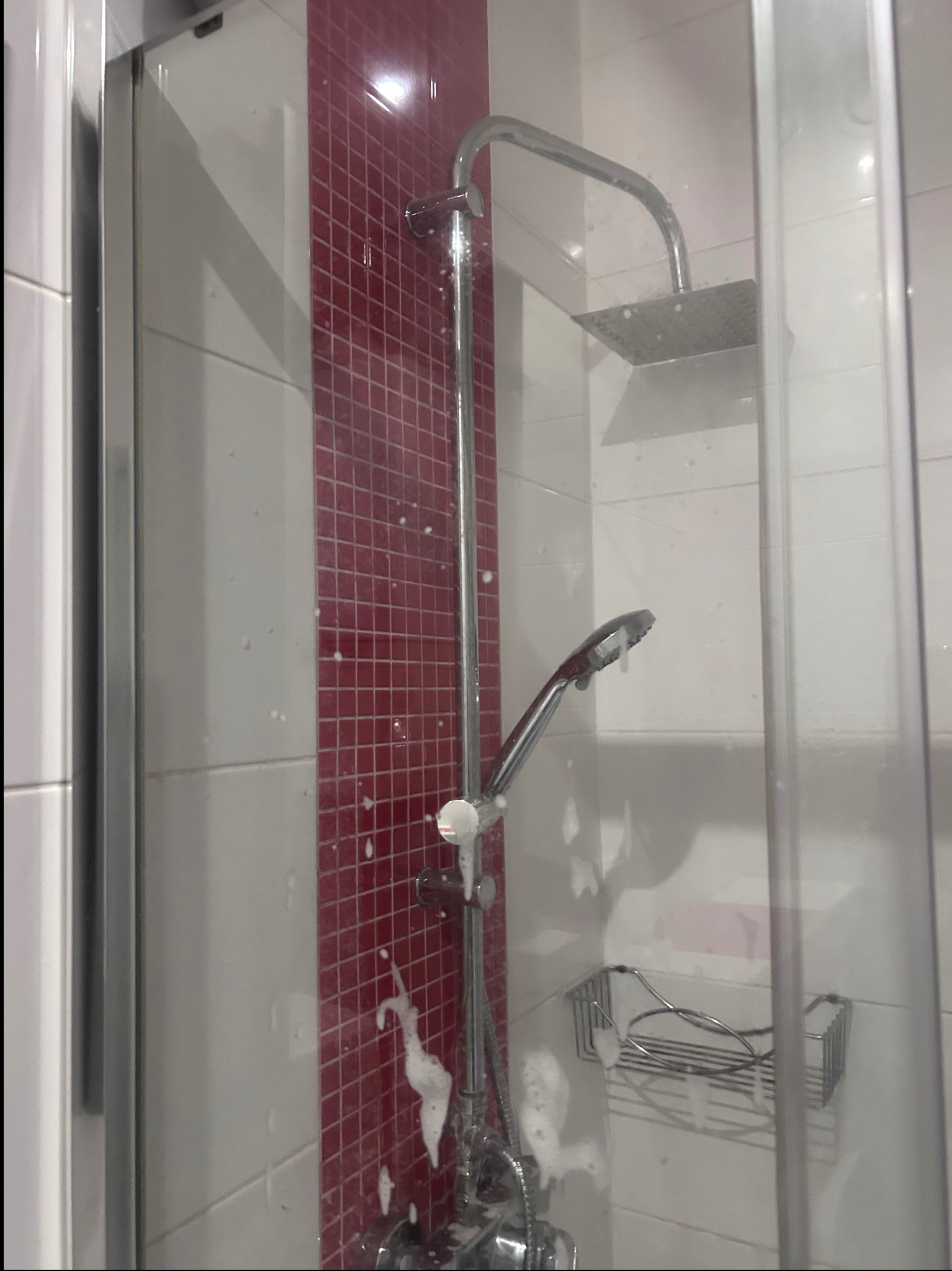 Kabina prysznicowa z czerwono-białymi płytkami po czyszczeniu, widoczne ślady piany po środku czyszczącym na ścianach i armaturze.