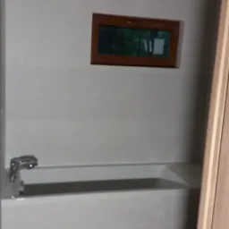 Biała wanna w wykończonej łazience z małym, prostokątnym oknem w drewnianej ramie i armaturą, widok na drewnianą podłogę ułożoną w jodełkę.