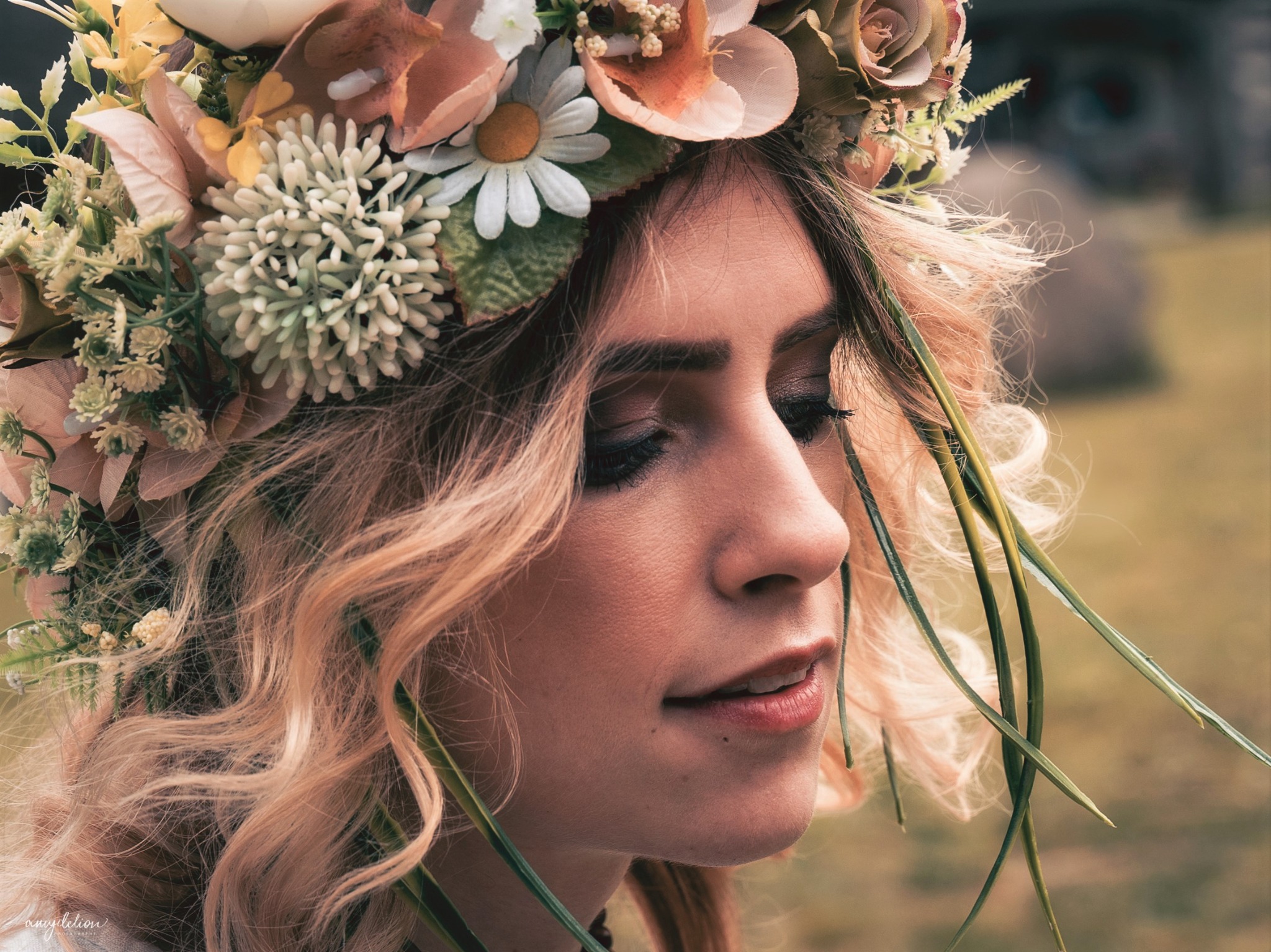 Portret kobiety z delikatnym makijażem oczu i ust, ozdobiona wiankiem z różnorodnych kwiatów i zielonych liści, uchwycona w profilu w naturalnym świetle.