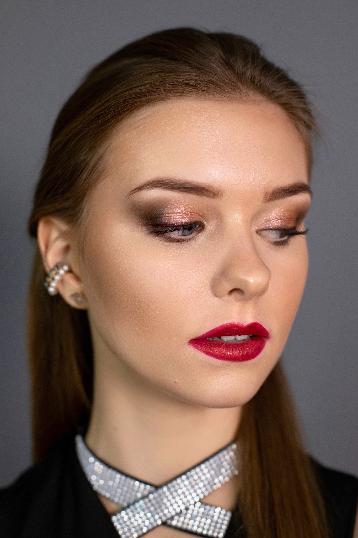 Portret kobiety z profesjonalnym makijażem: metaliczne cienie do powiek, mocne czerwone usta i perłowa kolczyka.