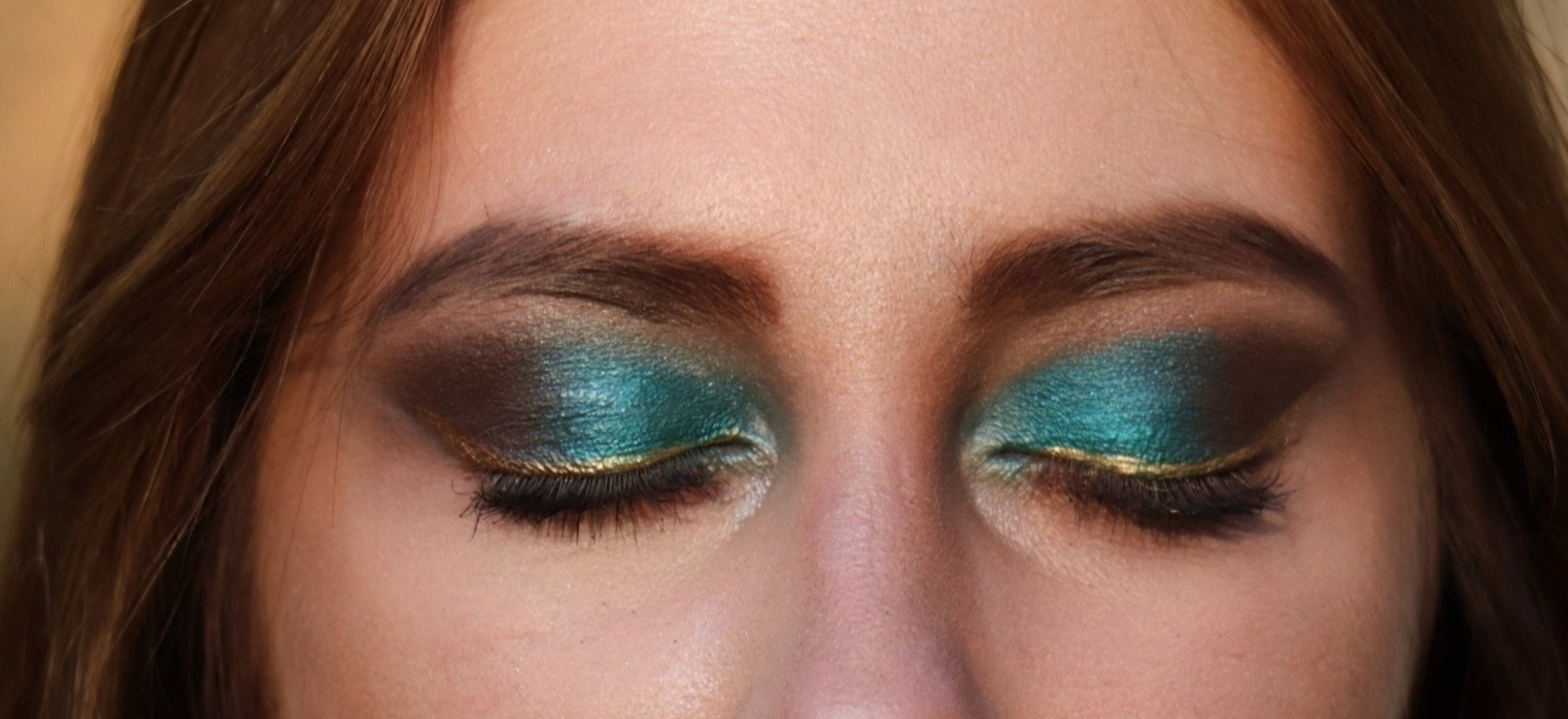 Zamknięte oczy z intensywnym, zielono-złotym makijażem smokey eye i brązowymi cieniami w zewnętrznym kąciku, podkreślone brwi.