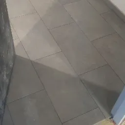 Ułożona szara podłoga z płytek w pomieszczeniu, widoczne pomarańczowe elementy dystansowe przy ścianie.