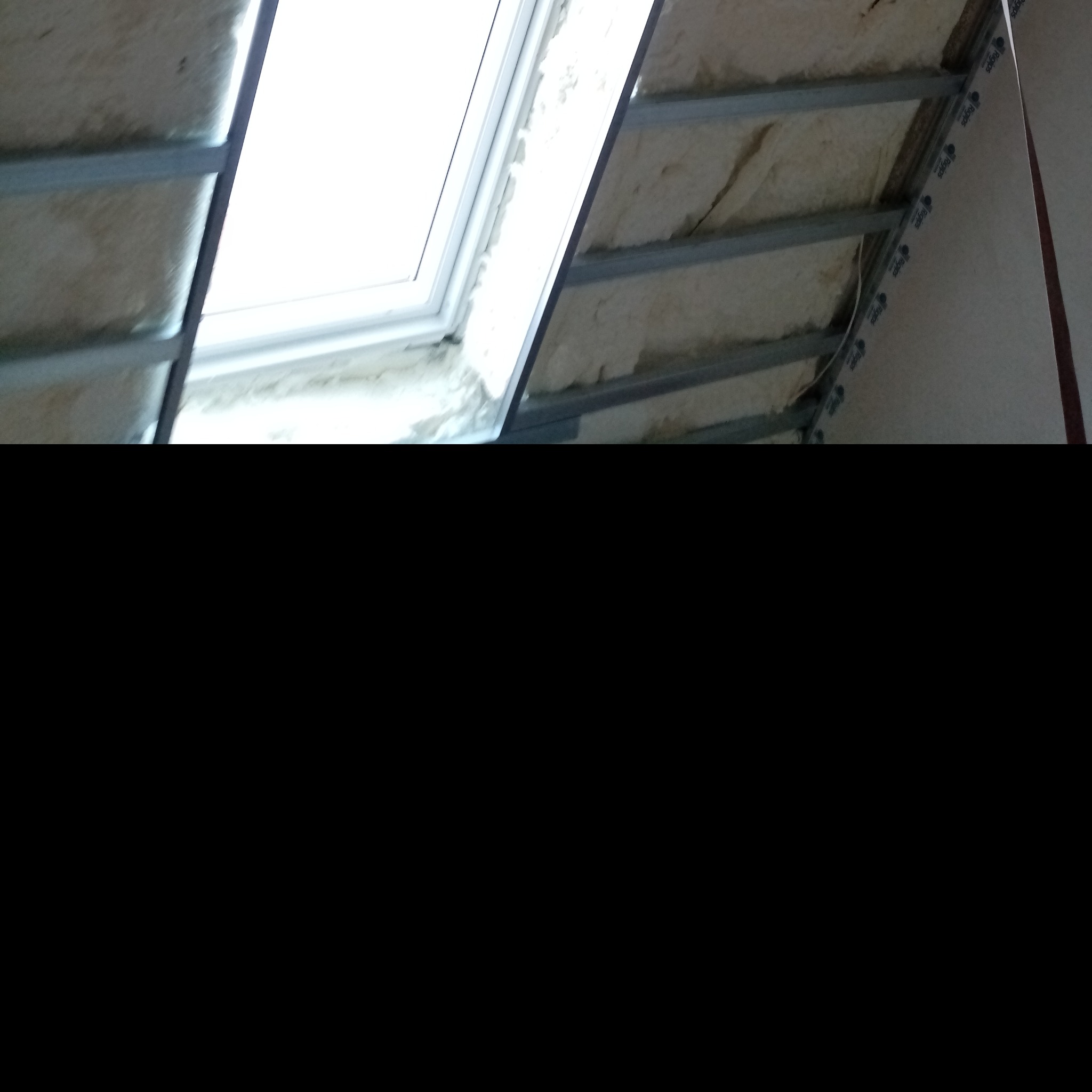 Montaż okna dachowego z izolacją z pianki i metalowym stelażem, widoczne płyty kartonowo-gipsowe marki Regips