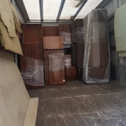 Wnętrze furgonetki transportowej wypełnionej meblami, w tym szafkami z ciemnego drewna i sofą owiniętą folią stretch, przygotowanymi do transportu.